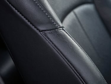 Macro shot of restored black leather grain on a car seat, dust-free stitching, illuminated by clinical white LED light, zero dust particles.