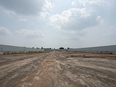 Wide ground-level shot of a cleared industrial plot at Savli GIDC, boundary walls visible, overcast daylight, open sky above, no people