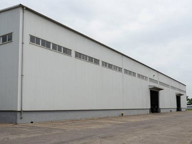 Ground-level facade of a large industrial warehouse building in an organised Gujarat industrial estate, overcast daylight, no signage, no people, clean documentary framing