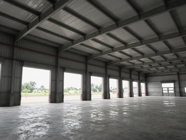 Wide interior shot of an empty warehouse unit with high ceiling, loading bay doors open to daylight, clean concrete floor, no people, overcast north-facing light, Gujarat industrial park setting