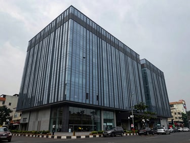 Exterior of a modern commercial office and retail block in Vadodara city centre, overcast daylight, glass facade, no people, wide documentary framing showing street context