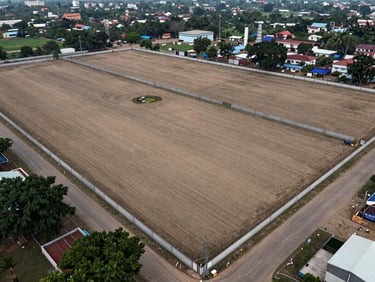 Aerial overhead view of a cleared industrial plot in Vadodara's GIDC zone, flat land marked with boundary walls, overcast daylight, no people