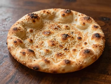 Close-up of a blistered, golden-brown Afghan flatbread with sesame seeds on a dark wooden table, warm side-lighting