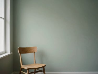 A quiet minimalist interior with soft north-facing daylight, a single empty wooden chair near a window casting gentle shadows on a sage green wall.