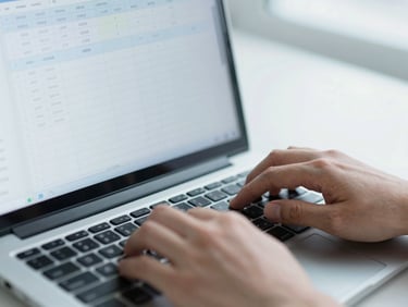 Close-up of hands typing on a keyboard, screen showing structured spreadsheets and clean code, soft cool daylight.