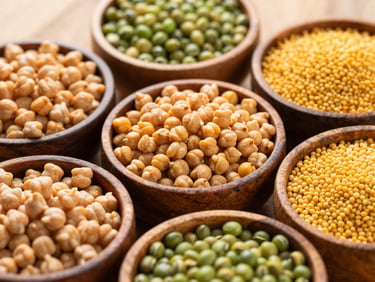 Assorted Indian pulses including chickpeas, lentils, green gram, and toor dal in rustic wooden bowls, warm golden tones, 35mm