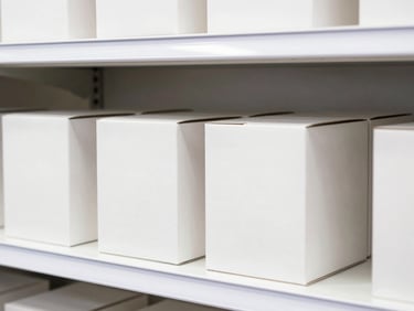 Neatly stacked premium packaging boxes on a clean white retail shelf, bright high-key lighting