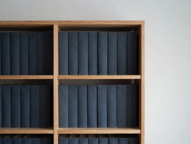 Plano medio de estanterías de madera con tomos académicos encuadernados en tonos oscuros, iluminación lateral suave, enfoque selectivo.