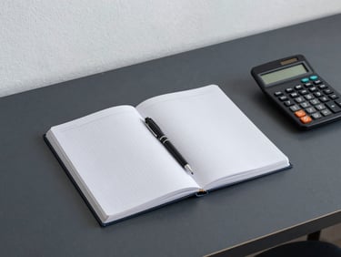 Plano cenital de un escritorio de trabajo minimalista con un cuaderno cuadriculado, un bolígrafo técnico y una calculadora científica, luz fría de estudio.
