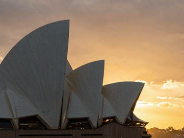 Sleek architectural details of the Sydney Opera House sails against a deep golden sunset sky.
