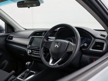 Detailed close-up of a modern black Honda hatchback dashboard and steering wheel, natural overcast daylight pouring through the windshield, clean interior.