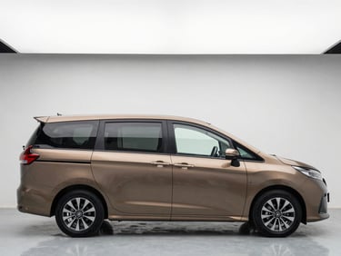 Eye-level side profile of a clean bronze Daihatsu family MPV parked in a minimalist showroom setting, bright white overhead lighting, neutral background.