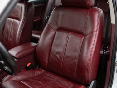 Close-up of a restored car seat in dark oxblood leather, precise topstitching visible under direct studio strobe, clean empty interior, no people