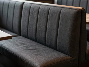 Empty restaurant booth with tight charcoal fabric upholstery, overhead daylight showing even seat padding and clean seam lines, no people, clean editorial shot