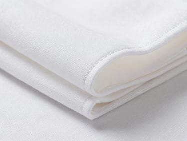 Close-up of tightly woven hospital-grade fabric — white polyester-cotton, visible tight weave structure under bright studio light, a folded stack showing clean seam lines, no people