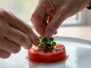 A close-up macro shot of hands carefully plating a delicate microgreen onto a rich red heirloom tomato dish, soft window light, shallow depth of field.