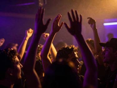 Dynamic low-angle shot of a crowd in motion blur under neon-violet and gold light leaks, hands raised, high-contrast club atmosphere, 35mm lens.