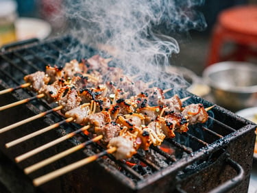 Close-up of pork skewers sizzling on a small charcoal grill on a Hanoi sidewalk, smoke rising, charred edges, warm flickering light, 35mm film style.