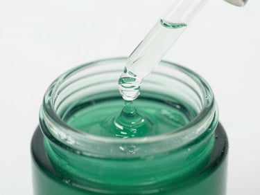 Close-up of a glass dropper dispensing clear viscous serum into an emerald green cosmetic jar, high-key laboratory lighting, sterile background