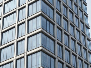 Exterior architectural detail of a high-end commercial building facade with glass panels reflecting bright daylight