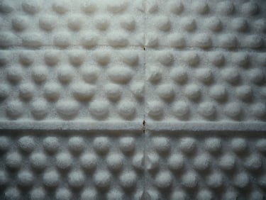 Overhead flatlay of rigid foam insulation panel showing uniform cell structure under cool studio light, gray and white tones, no people
