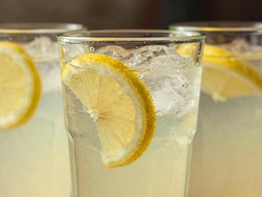 Close-up of a glass of freshly squeezed lemonade with lemon slices and ice, condensation on the glass, sun-drenched, nostalgic filter.