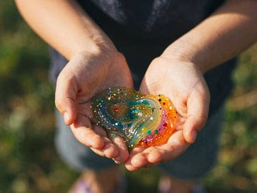 Child's hands stretching vibrant, colorful slime, with glitter and small beads mixed in, bright natural light, shallow depth of field.