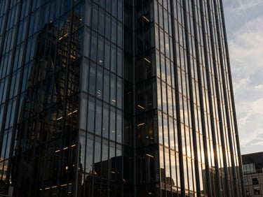 Architectural angle of a modern glass skyscraper in the City of London at golden hour, sharp lines, dramatic shadows, warm light reflecting off the facade.