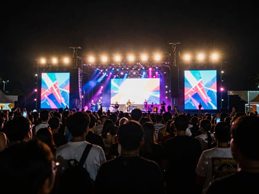 Vibrant neon stage lighting casting deep shadows over a crowded local music festival in Jakarta, wide concert shot, 35mm lens