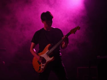 High-contrast dynamic shot of a guitarist performing live on a dark smoky stage with intense neon pink backlighting