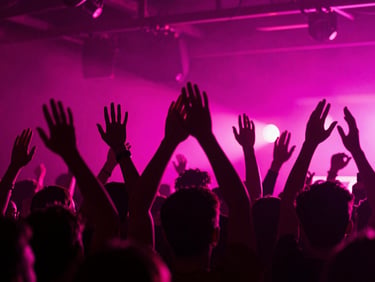 Dynamic crowd shot with hands raised under vibrant neon magenta stage lights, high-contrast editorial look