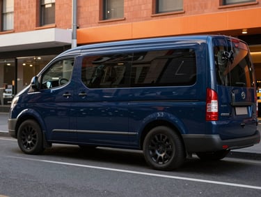 Wide environmental shot of a branded navy van parked on a recognizable Melbourne street, technician programming a car key, warm street lighting