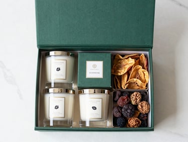 Top-down flat lay of a luxury corporate gift hamper containing artisan candles and premium dry fruits on a white marble surface