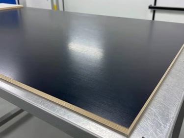 Close-up of a smooth, dark phenolic film faced plywood sheet, reflecting clean high-key technical lighting in a testing facility.