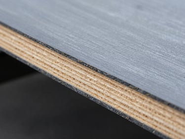Macro detail of the dark, sealed edge of a F17 formwork plywood sheet showing the distinct layered timber core, high-key technical lighting