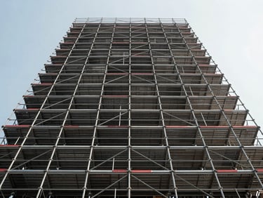 Symmetrical low-angle shot looking up at a massive, engineered steel scaffolding structure against a clear sky, highlighting precise load-bearing joints and safety boards.