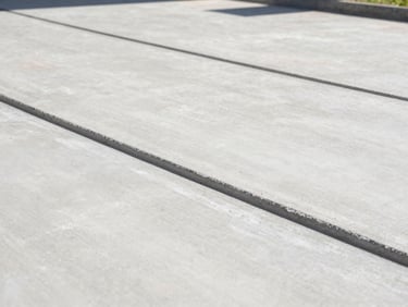 Low-angle architectural shot of a freshly poured reinforced concrete driveway with crisp clean edges and perfect joint cuts, bright morning sun highlighting the smooth texture, 35mm