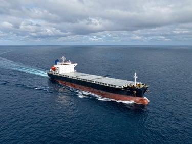 Wide-angle aerial view of a massive commercial tanker vessel cutting through deep blue ocean water under overcast maritime skies, dramatic lighting.