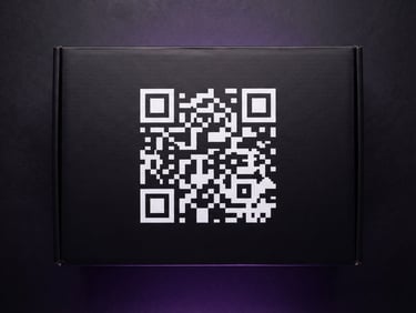 Overhead flat-lay of premium matte-black product packaging with a crisp, high-contrast custom QR code printed on the side, studio lighting, purple ambient glow