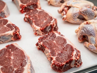 Medium close-up of fresh cuts of beef and poultry on clean white butcher paper, bright even commercial lighting, rich crimson tones, sharp focus