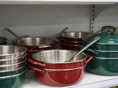 Clean commercial photography of stacked stainless steel kitchen pans and food prep tools on a metal shelf, bright even store lighting