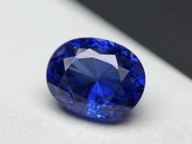 Macro photograph of an unset oval Ceylon sapphire on a white laboratory light table, studio strobes raking across the surface revealing the asterism and deep cornflower-blue saturation, sharp focus on the girdle facets