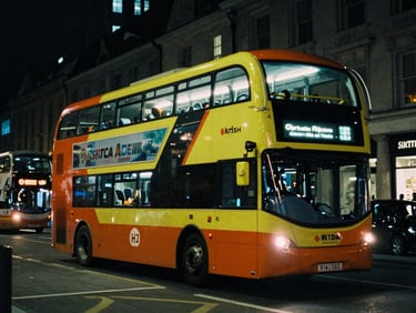 Cinematic night-time street shot of a branded double-decker bus glowing under city lights, moody atmosphere, 35mm film grain