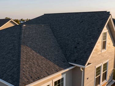 Wide ground-level shot of the same residential home after full roof replacement, crisp new dark architectural shingles, clean ridge, golden-hour light showing the finished surface