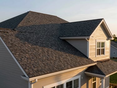 Wide ground-level shot of a completed full roof replacement on a two-story suburban home, new dark architectural shingles gleaming in golden-hour light, clean gutters and trim visible
