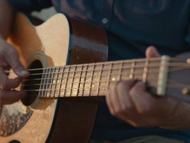 Extreme close-up of calloused hands on a worn guitar fretboard, warm sunset light glinting off brass frets, shallow depth of field.