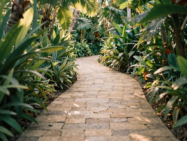 A winding garden path made of natural stone, surrounded by lush tropical plants, warm sunlight filtering through leaves, empty path.