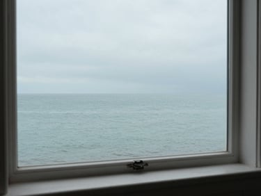 Panoramic overcast Normandy sea horizon from a window interior, pale light entering from the right, whitewashed wooden sill in foreground, empty calm water stretching to the horizon, muted celadon and grey tones