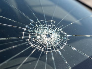 Macro close-up of a deep starburst windshield chip with radiating cracks, sharp glass texture, high-contrast California daylight reflections
