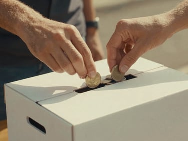 Close-up shot of hands gently placing coins into a donation box, warm nostalgic photography, soft golden hour light, faded vintage analog tones, 35mm film aesthetic, focus on the act of giving.